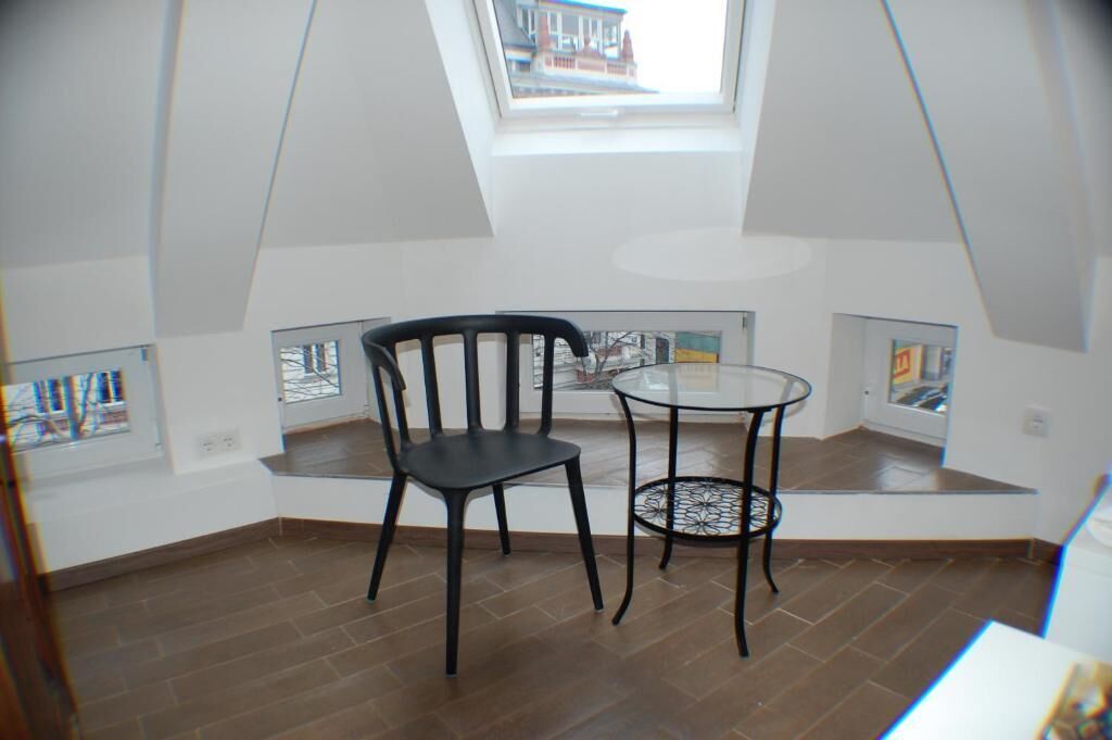 Een kamer met dakraam, een zwarte stoel, een klein rond tafeltje en uitzicht op buiten door een raam.