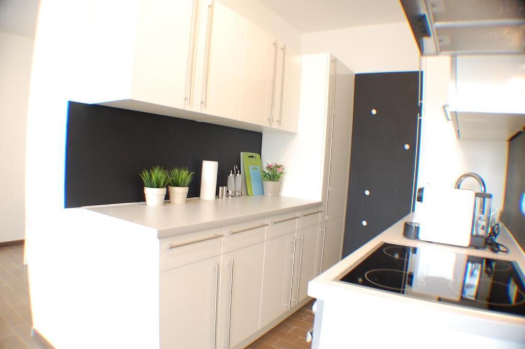 A modern kitchen with white cabinets, a black backsplash, and a stainless steel stove.