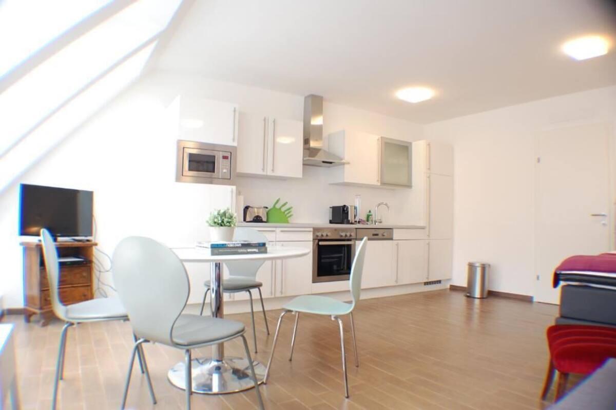 A modern kitchen with white cabinets, a microwave, stove, and a sink. There are two chairs and a table in the dining area.