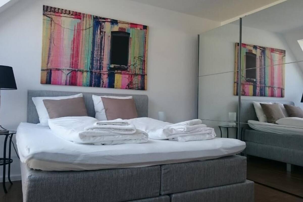 A modern bedroom with a bed, a bedside table, a lamp, and a large mirror.