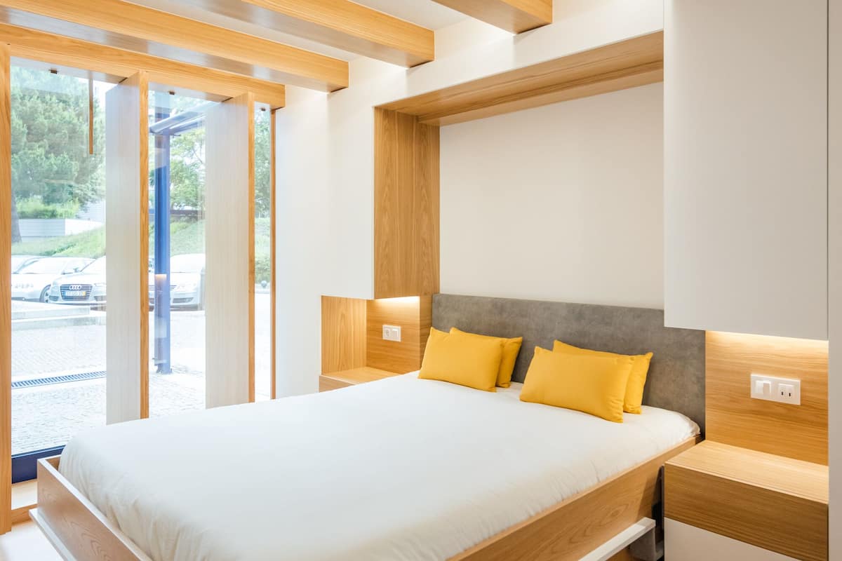Une chambre à coucher moderne avec une tête de lit en bois, un grand lit avec une literie blanche et une table de chevet avec une lampe.