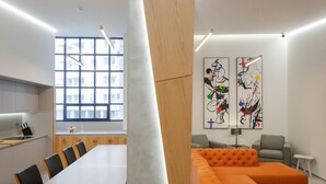 A modern interior with a long dining table, a large orange sectional sofa, and abstract art on the walls. - Sophia Oporto Urban Suites (Porto)
