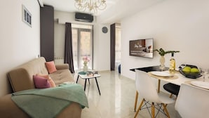 A modern living room with a sofa, a dining table with chairs, a chandelier, and a TV on the wall. - Stay Inn on Pushkin Street 43 (Yerevan)