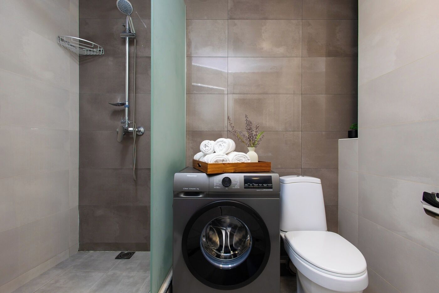 A compact bathroom with a washing machine, a toilet, and a shower.