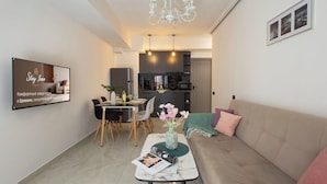 A modern living room with a sofa, a dining table with chairs, a TV mounted on the wall, and a kitchen in the background. - Stay Inn on Pushkin Street 43 (Yerevan)