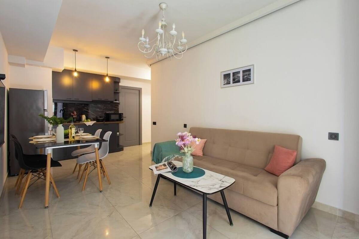 A modern living room with a sofa, dining table, chairs, and a chandelier.