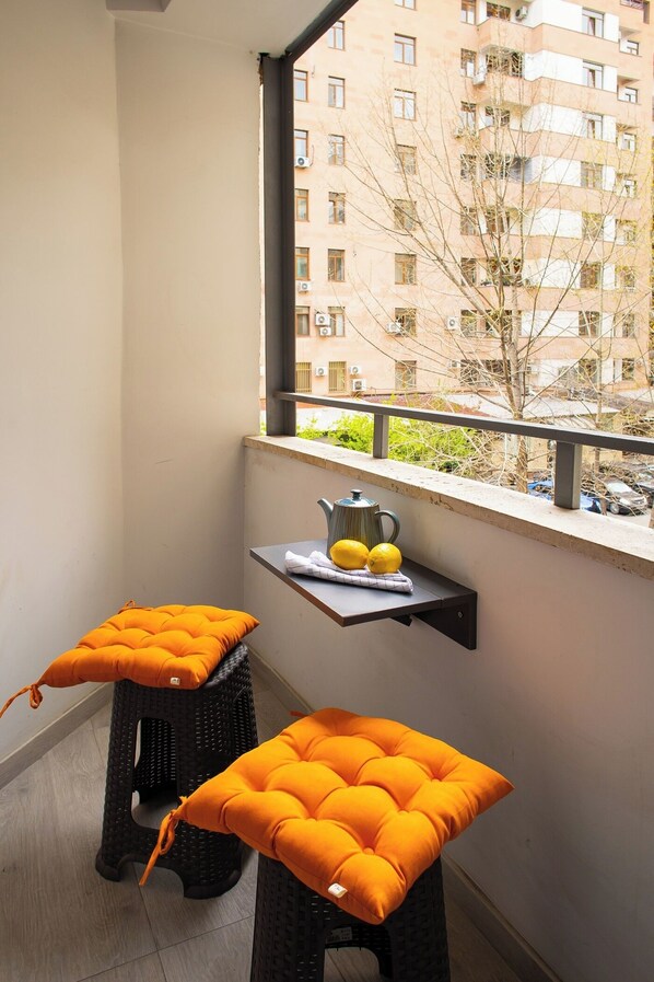 A balcony with two black stools, each with an orange cushion, and a small shelf with a teapot and lemons.