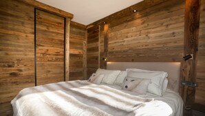 Un dormitorio con panel de madera en la pared, una cama con ropa de cama blanca y una mesita de noche con lámpara.