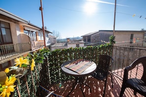 A balcony with a table and chairs, surrounded by greenery and a view of buildings.