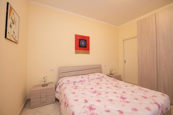 A bedroom with a bed, a nightstand, a wardrobe, and a wall-mounted artwork.