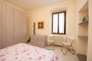 A bedroom with a bed, a dresser, a radiator, a window with curtains, and a bookshelf.