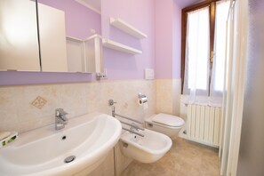 A bathroom with a sink, bidet, toilet, and a window with curtains.
