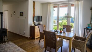 Una stanza accogliente con un tavolo in legno, sedie in vimini, una televisione e vista sul verde circostante.