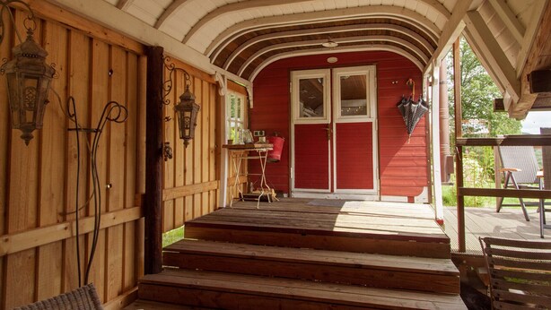 Un portico in legno con una porta rossa, un tavolino con degli oggetti e una panca.