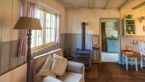 A cozy room with a checkered sofa, a wooden floor, a stove, and a kitchen area visible through an open door. - Stilles Glück Helmeroth (Helmeroth)