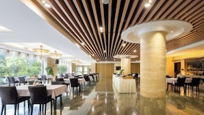 A spacious hotel lobby with a polished marble floor, modern wooden ceiling design, and a central column. Tables and chairs are arranged for dining. - Nanyue Resort (Huoshan)