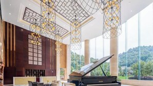 A grand lobby with a grand piano, modern chandeliers, and a large window offering a scenic view. - Nanyue Resort (Huoshan)