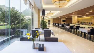 A restaurant with a long table, chairs, and a vase of yellow flowers.