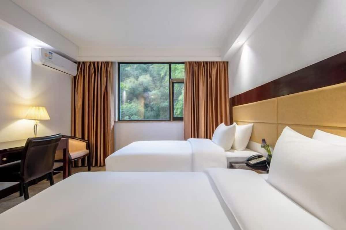 A hotel room with two beds, a desk, a lamp, and a window with curtains.