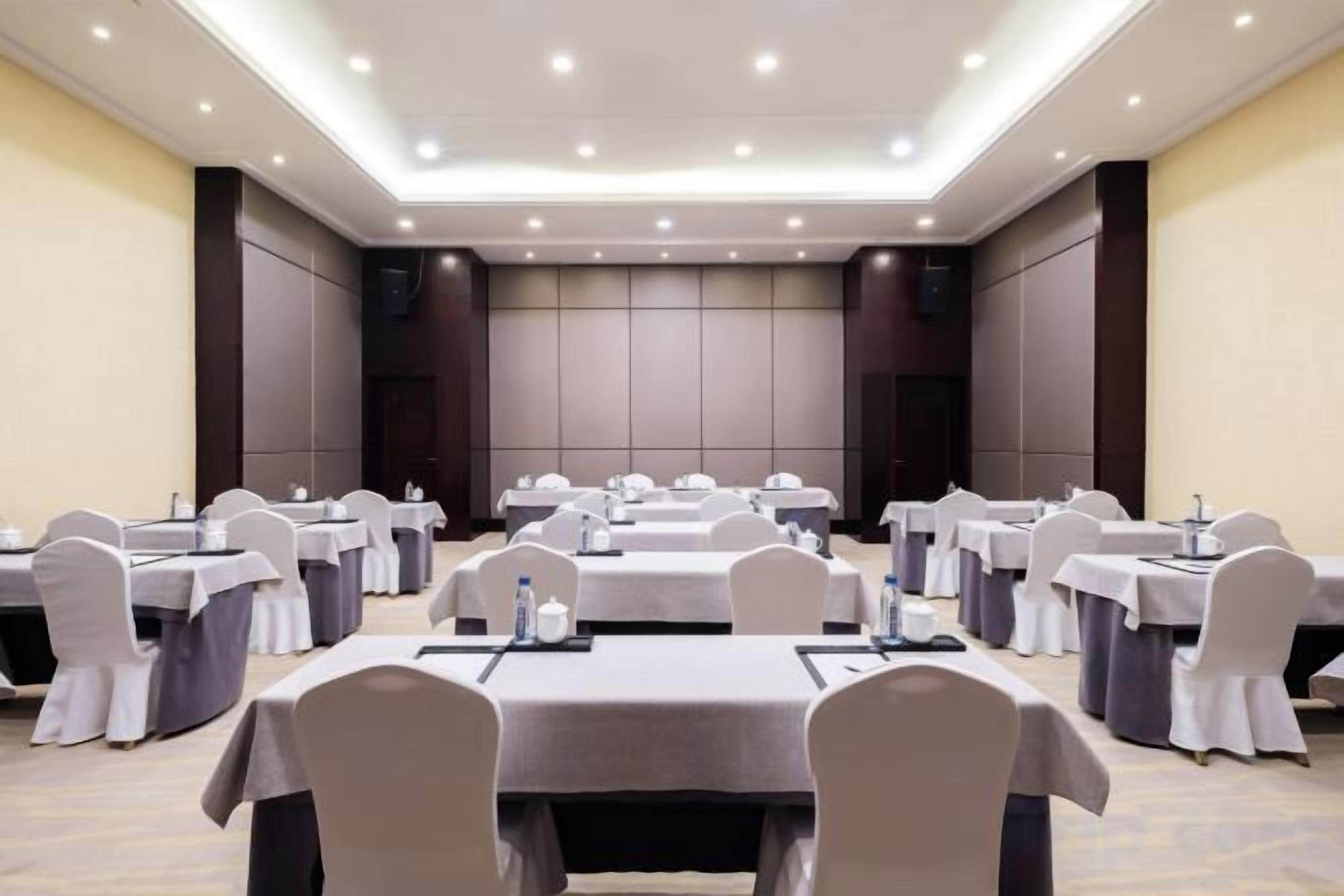 A conference room with multiple tables and chairs, equipped with microphones and water bottles.