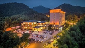 A hotel with multiple buildings, a parking lot, and a mountainous backdrop. - Nanyue Resort (Huoshan)