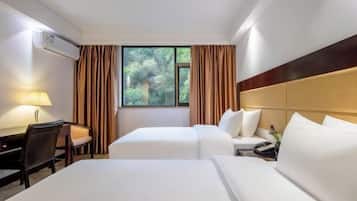 A hotel room with two beds, a desk, a lamp, and a window with curtains.