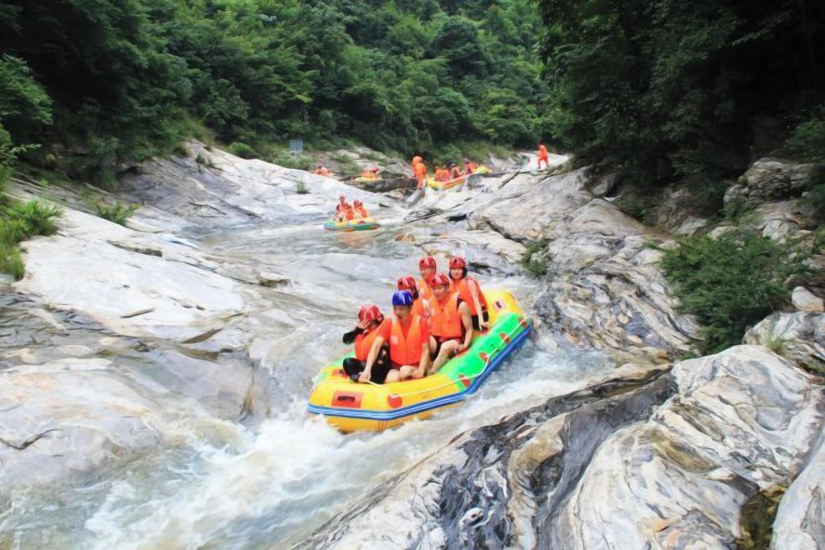 A group of people rafting down a river surrounded by rocky terrain and greenery.
