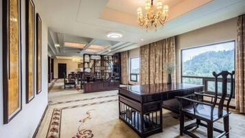 A spacious room with a large desk, chairs, a chandelier, and a view of a mountainous landscape.