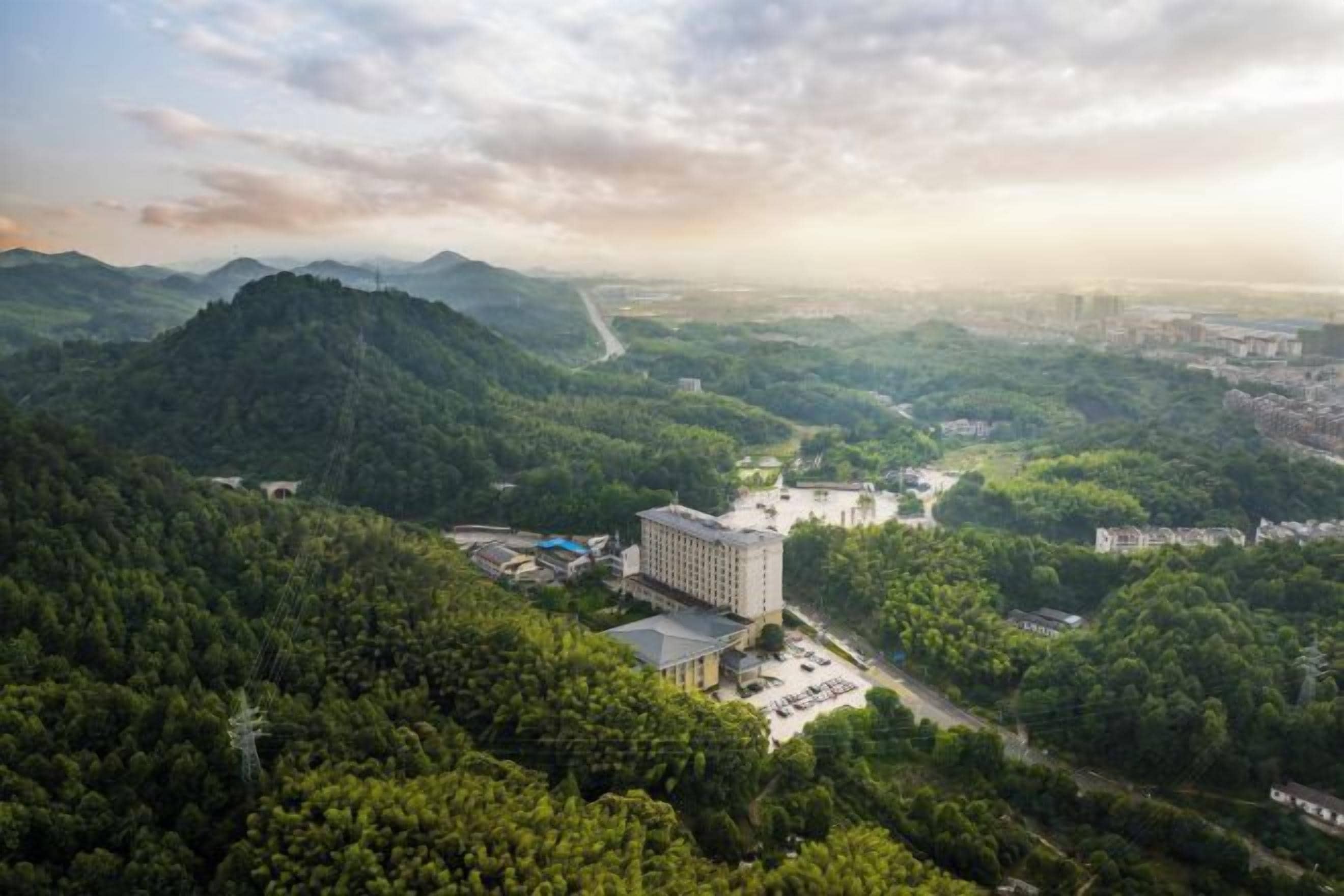 A hotel surrounded by lush greenery with a view of a valley and distant cityscape.