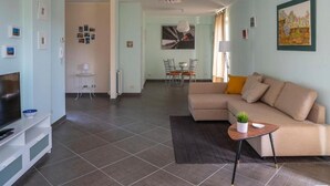 A modern living room with a sofa, TV, and a dining area with chairs and a table.