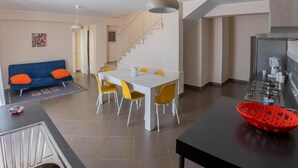 A modern living space with a dining area, sofa, staircase, and kitchen.