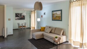 A modern living room with a sectional sofa, a dining area with chairs, a small side table with a plant, and artwork on the walls.