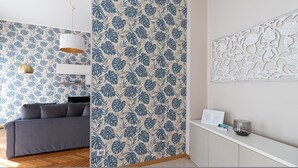 A room with a grey sofa, a white cabinet, and a wall with a blue and beige leaf pattern. - Italianway Collection - Cannobio 8 - Trovatore (Milan)