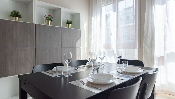 A modern dining area with a dark wooden table set for four, surrounded by grey cabinets and potted plants. - Italianway Collection - Cannobio 8 - Trovatore (Milan)
