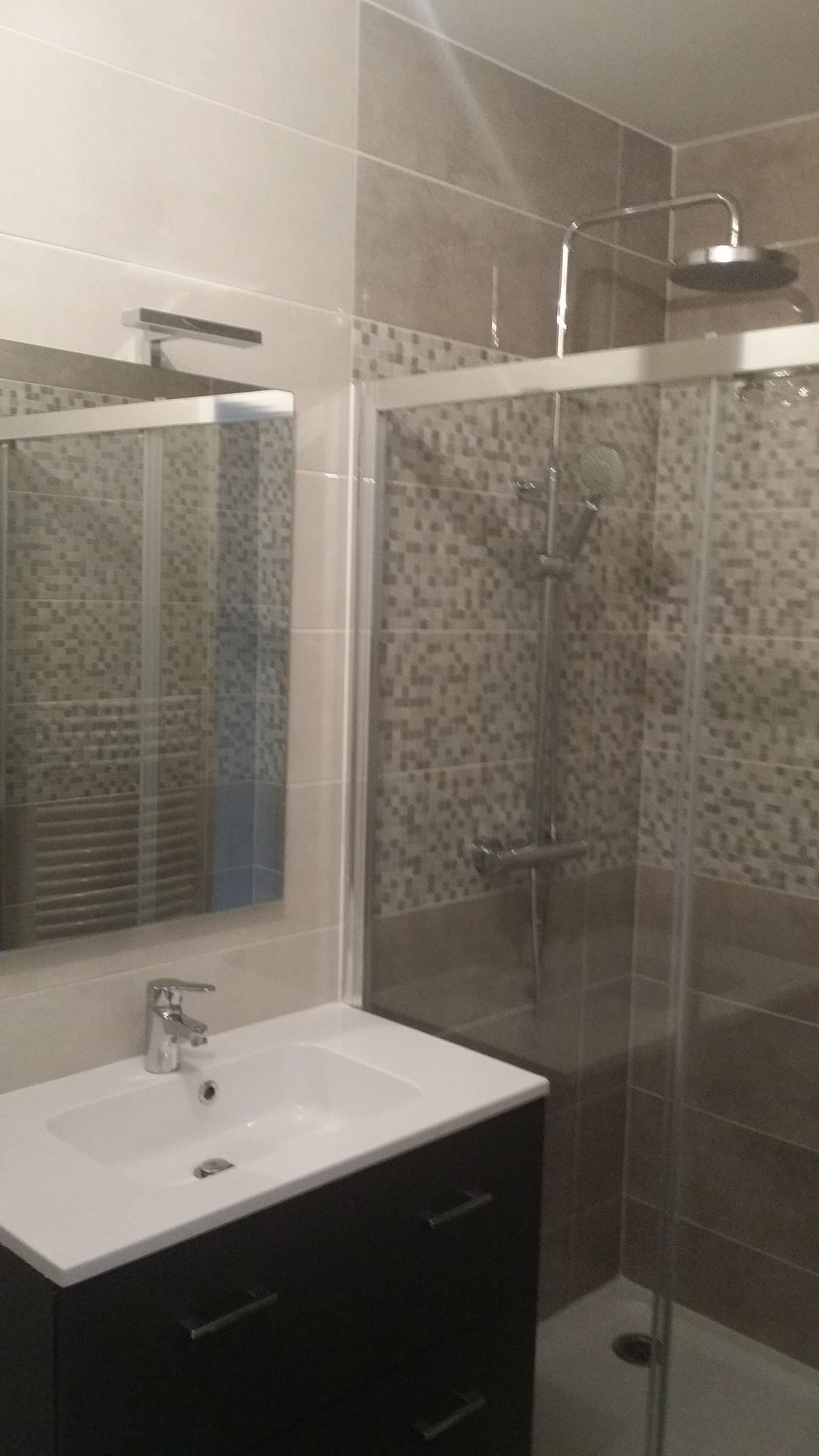 A bathroom with a white sink, a mirror, a shower with a glass door, and tiled walls.