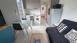 A compact living space with a sofa, a small table, a washing machine, and a kitchenette. - Aix-les-Bains Grand Port T2 Furnished 3 Stars Terrace 57m2 (Aix-les-Bains)