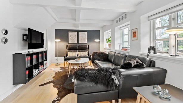 A modern living room with a leather sofa, a flat-screen TV, a bookshelf, and a large window with natural light. - Stunning home in Nørre Nebel (Nørre Nebel)