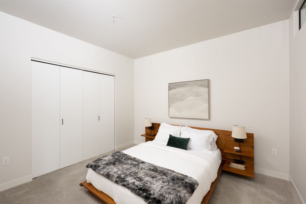 Une chambre à coucher comprenant un lit, une table de chevet, une lampe fixée au mur, un tableau et une armoire.