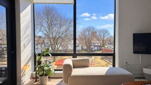 Ein modernes Wohnzimmer mit großem Fenster, einem beigen Sofa, einem kleinen Tisch und einem Blumentopf.