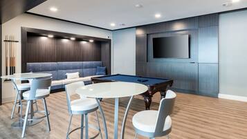Una sala de estar moderna con una mesa de billar, un sofá y un televisor montado en la pared.
