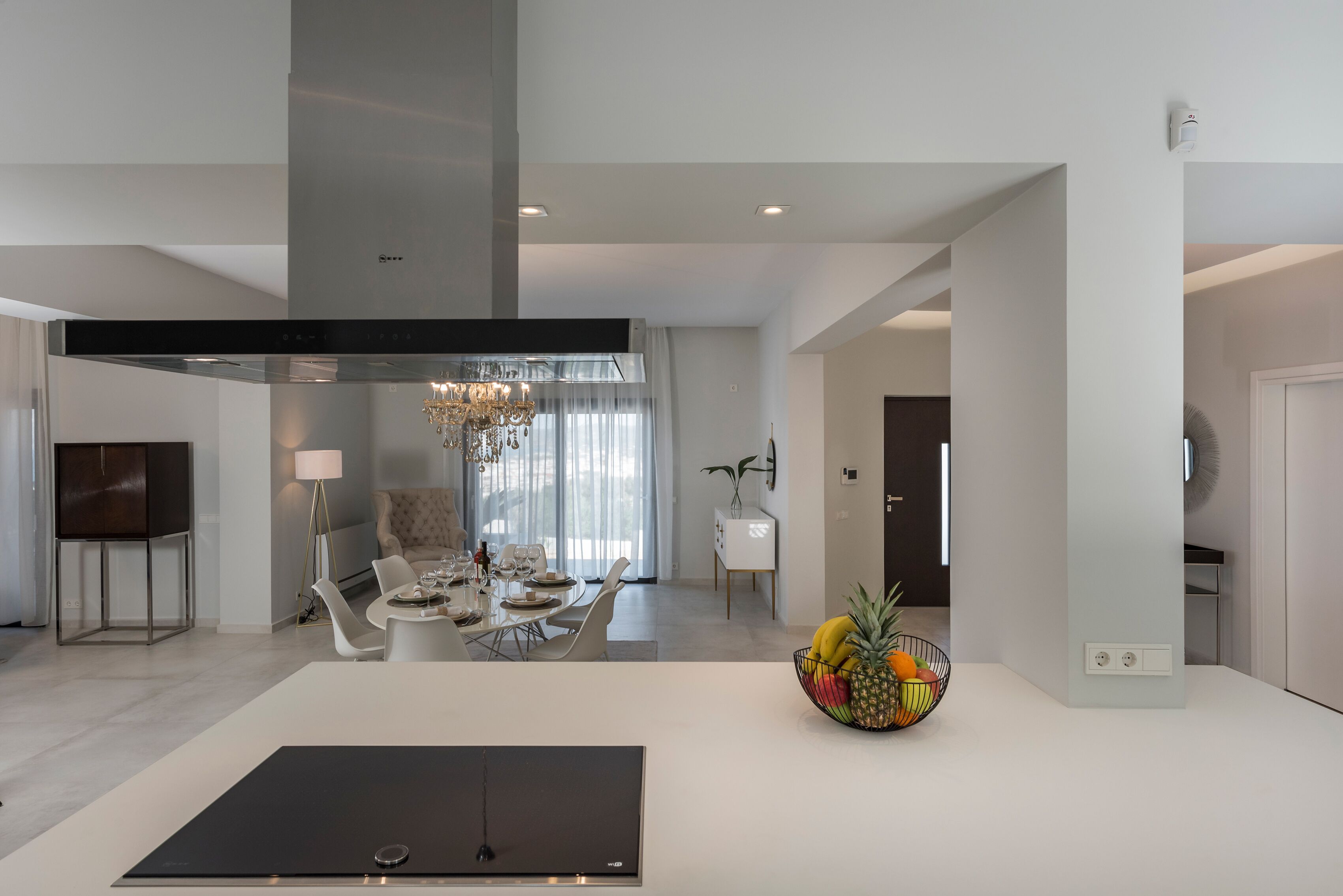 Una cocina moderna con una isla central, un comedor con candelabro, y un frutero en la isla.