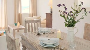 Een eetgedeelte met een houten tafel voor vier personen, een bloevas en uitzicht op het strand door het raam.
