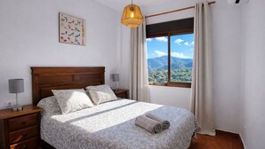 A bedroom with a wooden headboard, two bedside tables with lamps, a patterned bedspread, a window with a mountain view, and a hanging light fixture. - Torcal 1 - Magnificent Villa for 8 People, Heated Pool, A/C, WIFI, Pet friendly! (Comares)