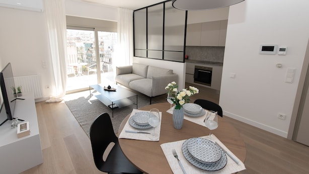 Een moderne woonkamer met een bank, een eettafel gedekt met borden en een bloevas.