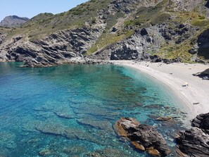 En kyststrækning med krystalklart turkis vand, klippekyster og et sandstrand.