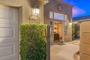 Une maison avec une porte de garage, une haie bien entretenue et une vue dégagée sur l’intérieur grâce à la porte ouverte.