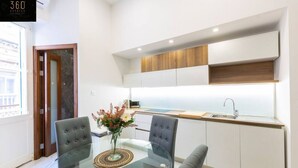 A modern kitchen with white cabinets, a wooden countertop, and a glass dining table with two chairs. - Designer APT on Sliema Promenade, Perfect Location (Tas-Sliema)