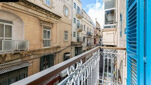 A narrow street with buildings on either side, a balcony with ornate metal railings, and a blue shutter on the right. - Designer APT on Sliema Promenade, Perfect Location (Tas-Sliema)