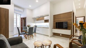 A modern living room with a sofa, a dining area with chairs and a table, a kitchen with cabinets and a TV, and a wooden accent wall. - Designer APT on Sliema Promenade, Perfect Location (Tas-Sliema)