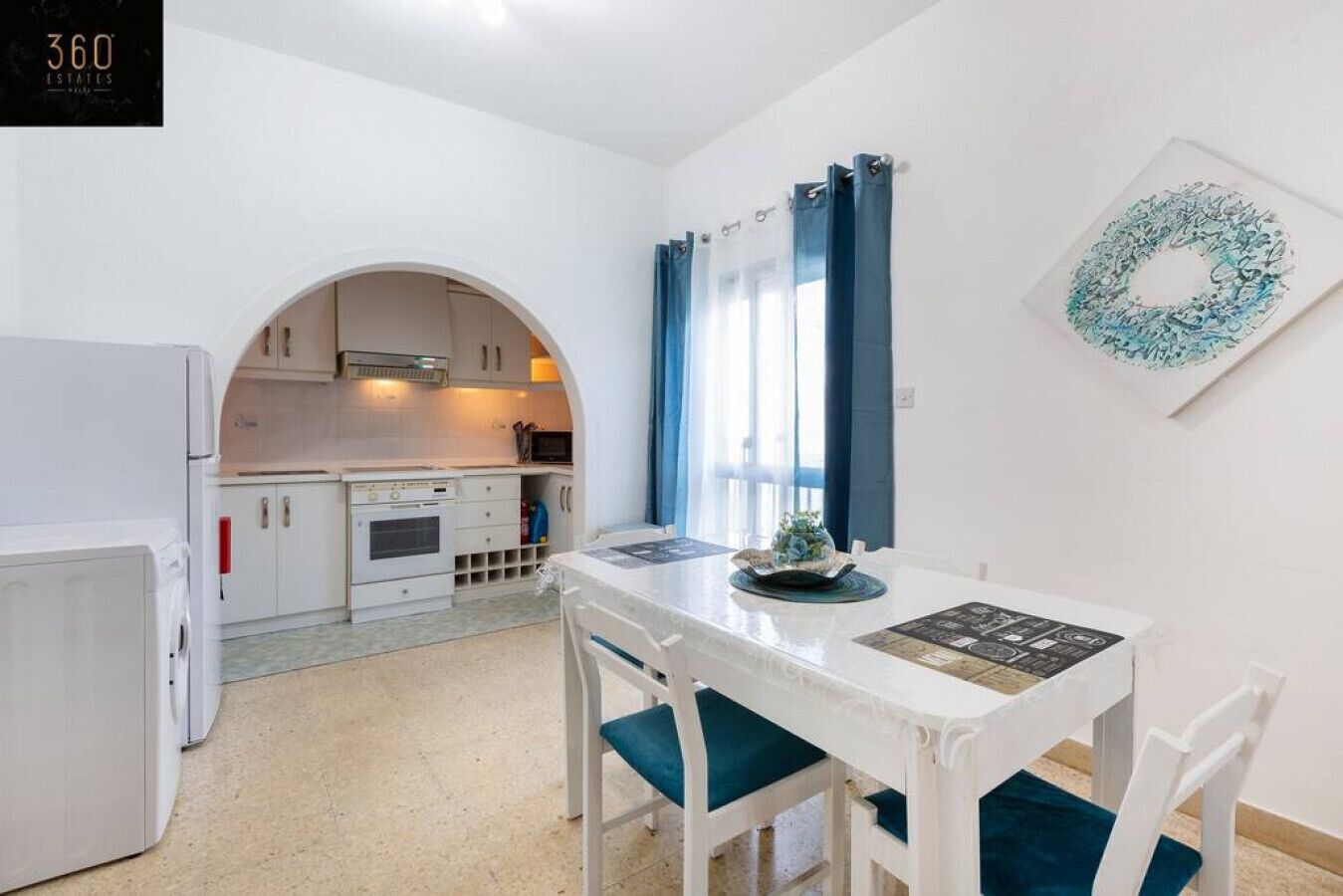 A compact kitchen with white cabinets, a white refrigerator, and a dining table with blue chairs.